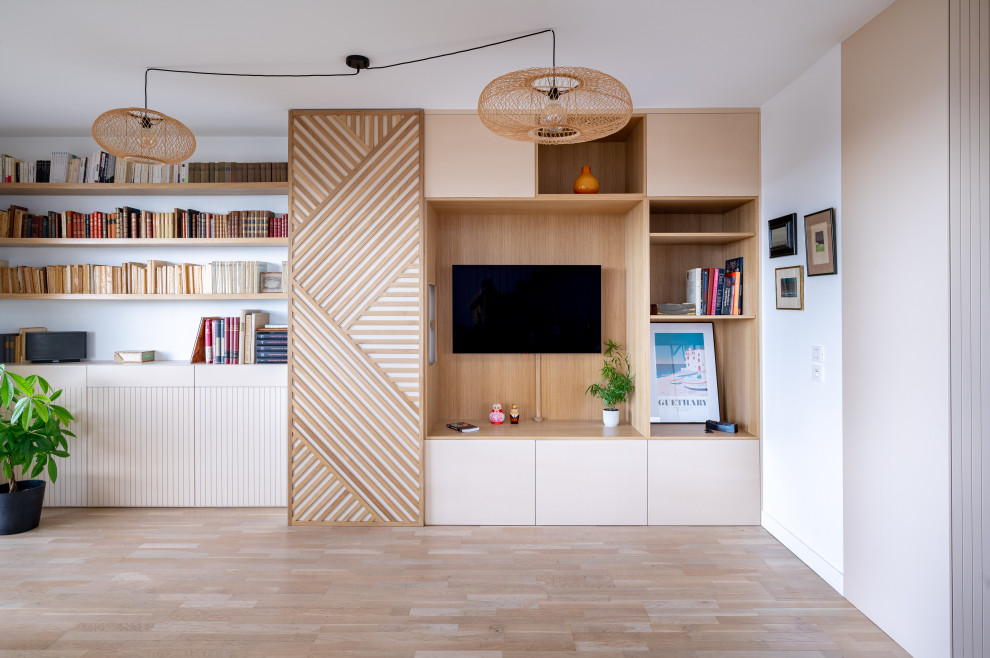 Cette photo montre un grand salon scandinave en bois ouvert avec une bibliothèque ou un coin lecture, un mur beige, parquet clair et un téléviseur fixé au mur.
