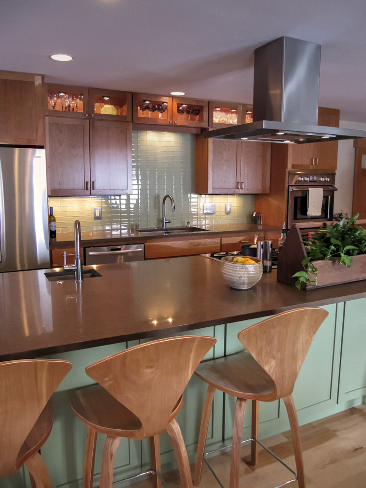Example of a mid-sized transitional galley light wood floor kitchen design with quartz countertops, glass tile backsplash, stainless steel appliances, an undermount sink, shaker cabinets, green cabinets, an island and green backsplash