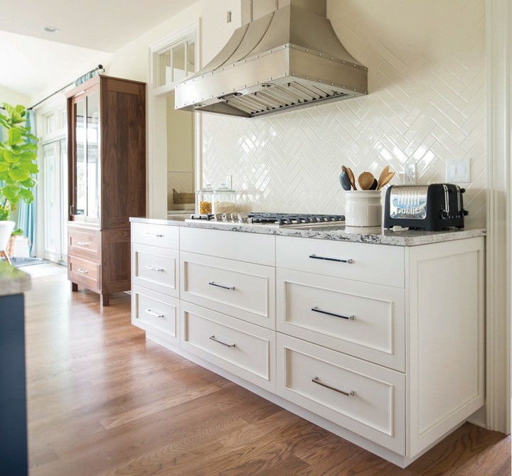 This is an example of a large transitional l-shaped open plan kitchen in Boston with an undermount sink, recessed-panel cabinets, white cabinets, marble benchtops, white splashback, ceramic splashback, stainless steel appliances, light hardwood floors and with island.