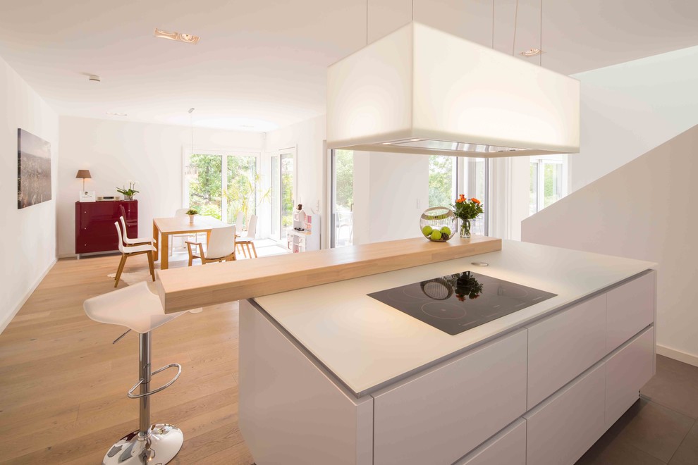 This is an example of a mid-sized modern open plan kitchen in Other with white cabinets, grey splashback, light hardwood floors, with island, brown floor, grey benchtop and flat-panel cabinets.
