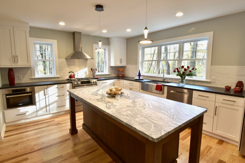 Inspiration for a mid-sized contemporary l-shaped open plan kitchen in Boston with a farmhouse sink, flat-panel cabinets, white cabinets, granite benchtops, white splashback, ceramic splashback, stainless steel appliances, medium hardwood floors, with island and black benchtop.