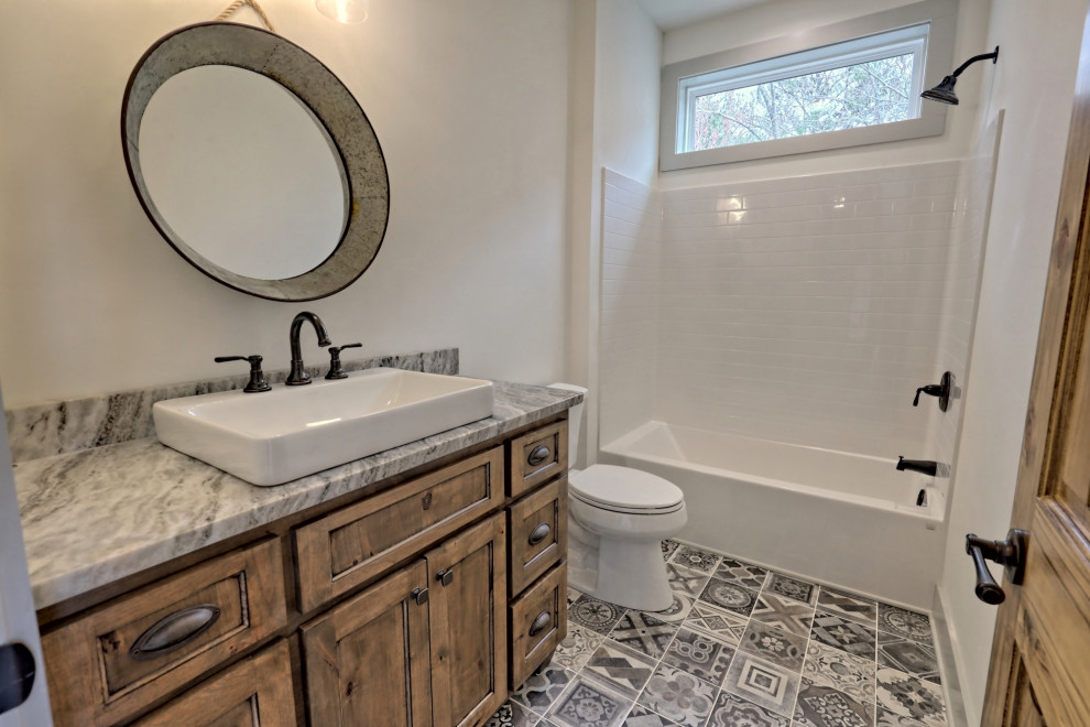 Photo of a mid-sized country bathroom in Atlanta with shaker cabinets, medium wood cabinets, an alcove tub, a shower/bathtub combo, a two-piece toilet, white walls, ceramic floors, a vessel sink, granite benchtops, multi-coloured floor, a shower curtain, multi-coloured benchtops, a single vanity and a built-in vanity.