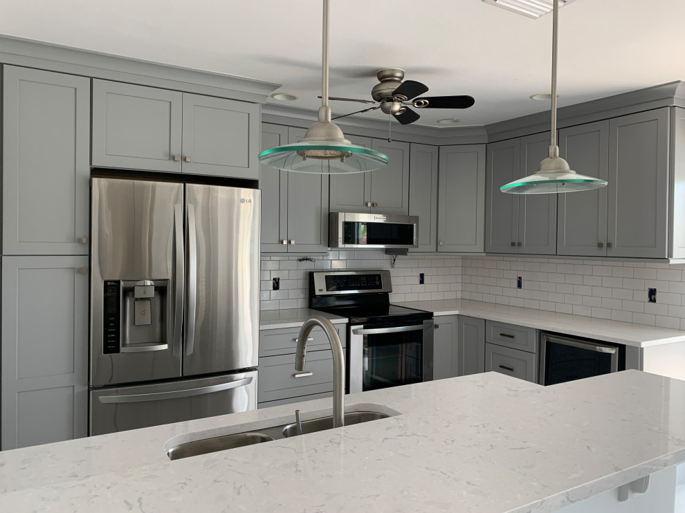 This is an example of a mid-sized transitional l-shaped open plan kitchen in Miami with an undermount sink, flat-panel cabinets, grey cabinets, quartz benchtops, white splashback, ceramic splashback, stainless steel appliances, porcelain floors, a peninsula, white floor and white benchtop.