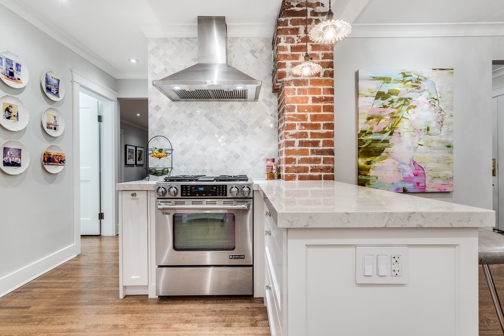 This is an example of a mid-sized traditional l-shaped eat-in kitchen in Vancouver with a farmhouse sink, shaker cabinets, white cabinets, quartz benchtops, grey splashback, stone tile splashback, stainless steel appliances, medium hardwood floors and a peninsula.
