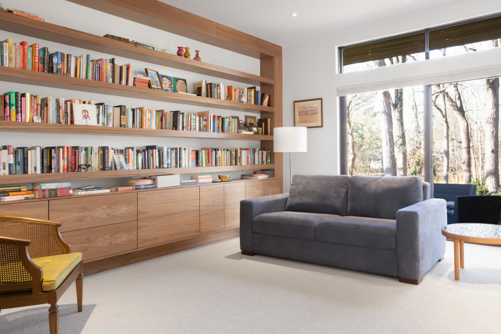 Aménagement d'une salle de séjour moderne ouverte avec une bibliothèque ou un coin lecture, un mur blanc, moquette et un sol beige.