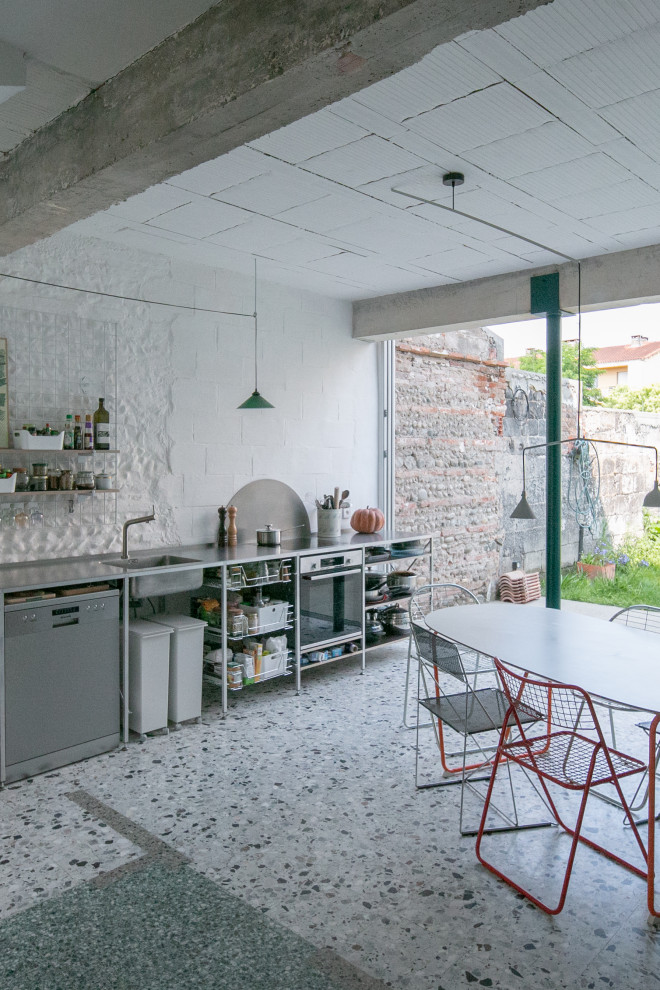 Foto på ett industriellt grå linjärt kök och matrum, med en integrerad diskho, öppna hyllor, bänkskiva i rostfritt stål, rostfria vitvaror, terrazzogolv och grått golv