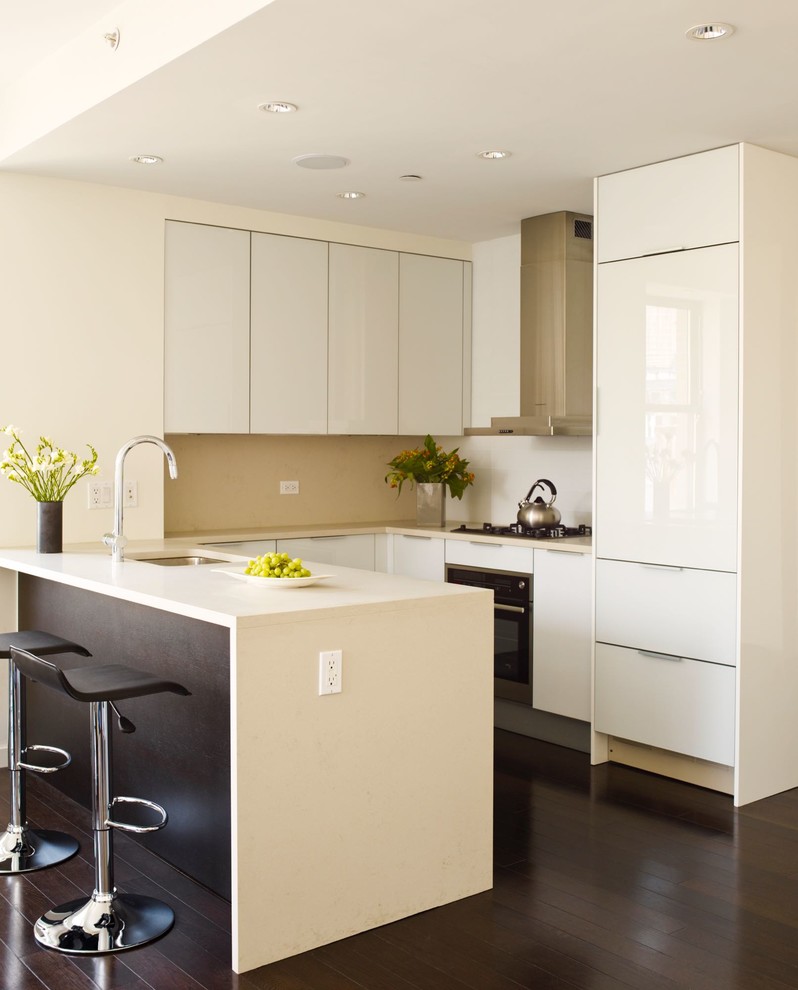 This is an example of a small modern u-shaped eat-in kitchen in New York with an undermount sink, flat-panel cabinets, white cabinets, quartz benchtops, beige splashback, stone slab splashback, stainless steel appliances, dark hardwood floors, a peninsula, brown floor and white benchtop.
