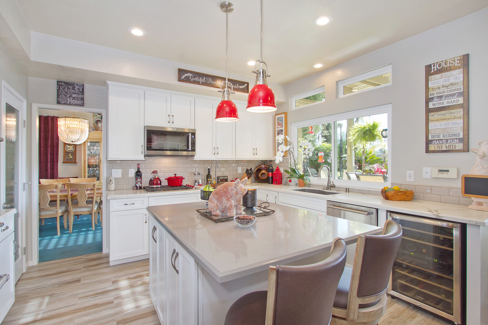 Photo of a large modern u-shaped eat-in kitchen in San Diego with a drop-in sink, recessed-panel cabinets, white cabinets, quartzite benchtops, beige splashback, subway tile splashback, stainless steel appliances, painted wood floors, with island and brown floor.
