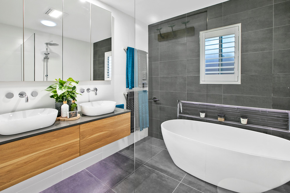 Photo of a mid-sized contemporary master wet room bathroom in Sydney with furniture-like cabinets, medium wood cabinets, a freestanding tub, a one-piece toilet, white tile, ceramic tile, grey walls, ceramic floors, a vessel sink, engineered quartz benchtops, grey floor, an open shower and grey benchtops.