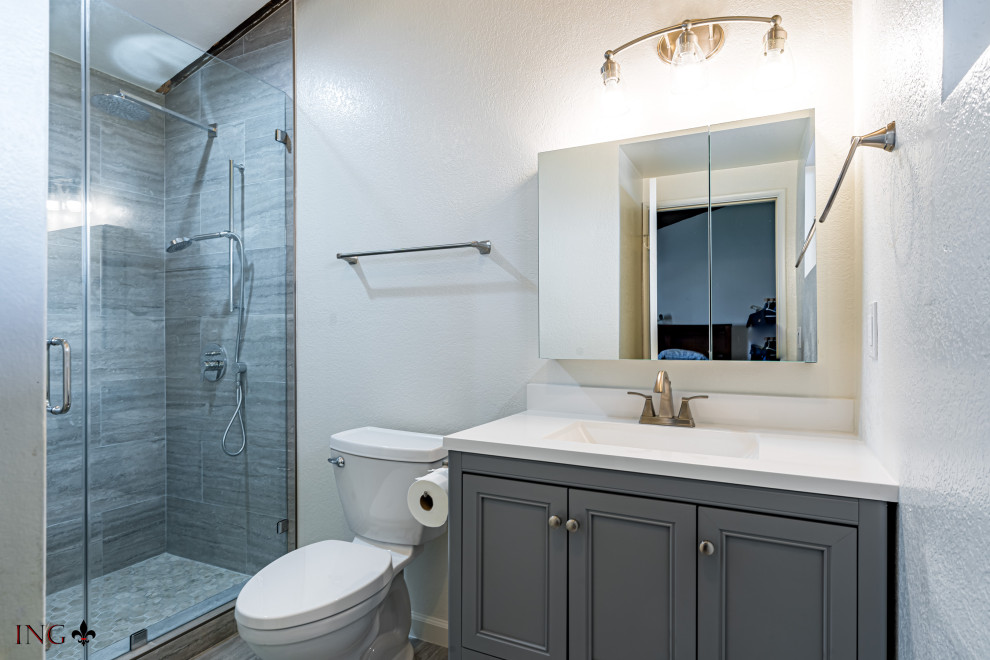 Mid-sized trendy 3/4 gray tile and cement tile single-sink, gray floor and ceramic tile corner shower photo in Los Angeles with shaker cabinets, gray cabinets, a two-piece toilet, an undermount sink, granite countertops, a hinged shower door, white countertops, a niche, a freestanding vanity and white walls