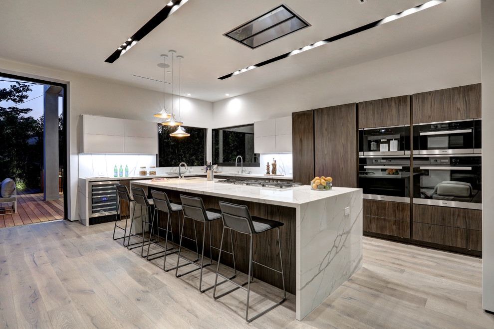 Inspiration for a contemporary kitchen in Los Angeles with an undermount sink, flat-panel cabinets, dark wood cabinets, white splashback, black appliances, light hardwood floors, with island and beige floor.