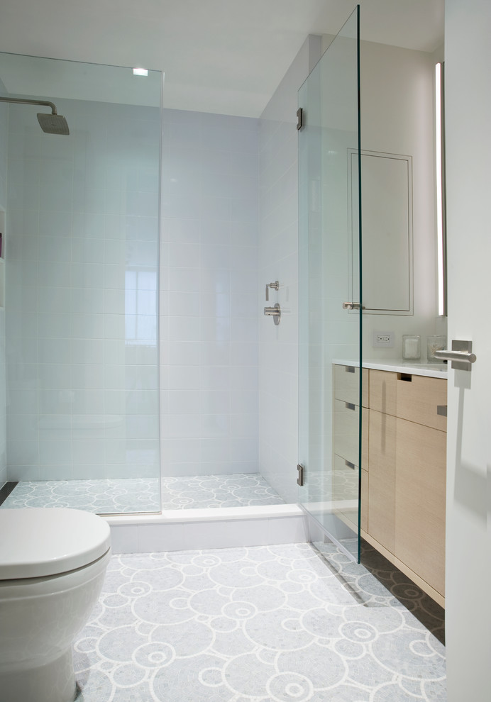 Photo of a mid-sized contemporary master bathroom in New York with an undermount sink, flat-panel cabinets, light wood cabinets, engineered quartz benchtops, an alcove shower, a one-piece toilet, white tile, glass tile, white walls and mosaic tile floors.