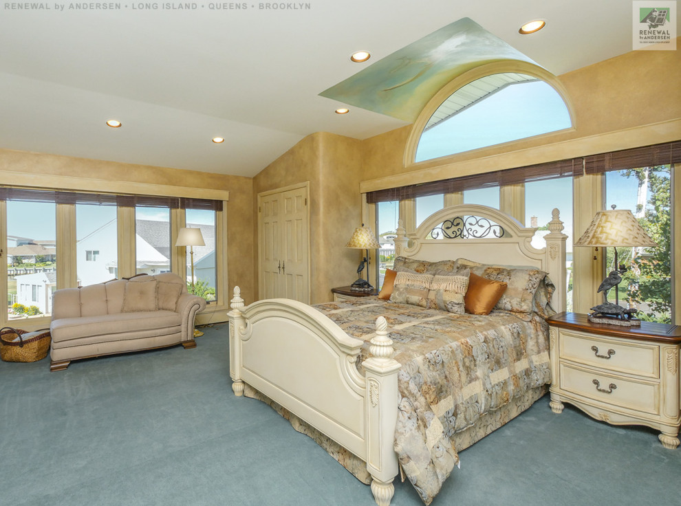 Großes Hauptschlafzimmer ohne Kamin mit beiger Wandfarbe, Teppichboden, blauem Boden, gewölbter Decke und Tapetenwänden in New York