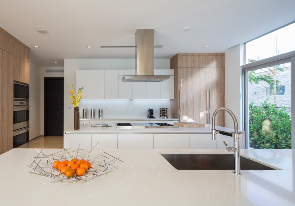 Inspiration for a mid-sized contemporary kitchen in Miami with a drop-in sink, flat-panel cabinets, white cabinets, wood benchtops, white splashback, panelled appliances, porcelain floors, multiple islands, beige floor and beige benchtop.