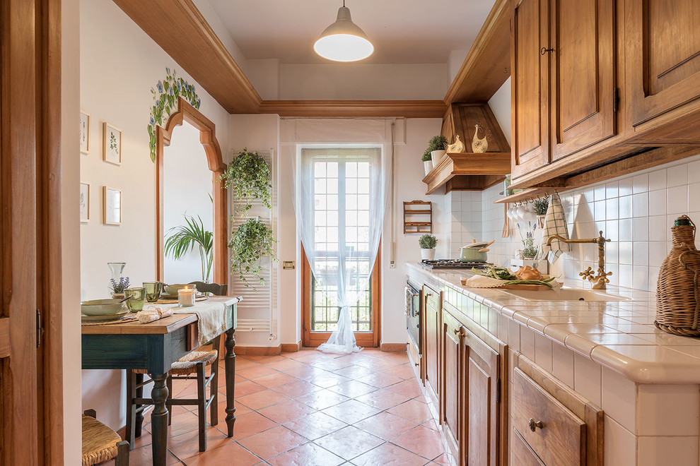 Mediterranean single-wall eat-in kitchen in Rome with a drop-in sink, raised-panel cabinets, medium wood cabinets, white splashback, panelled appliances, terra-cotta floors, no island, orange floor and beige benchtop.