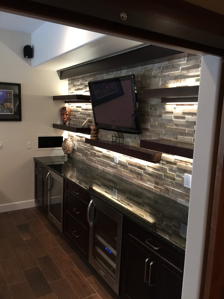 This is an example of a mid-sized transitional single-wall seated home bar in Denver with dark wood cabinets, grey splashback, stone tile splashback, porcelain floors, an undermount sink and black benchtop.