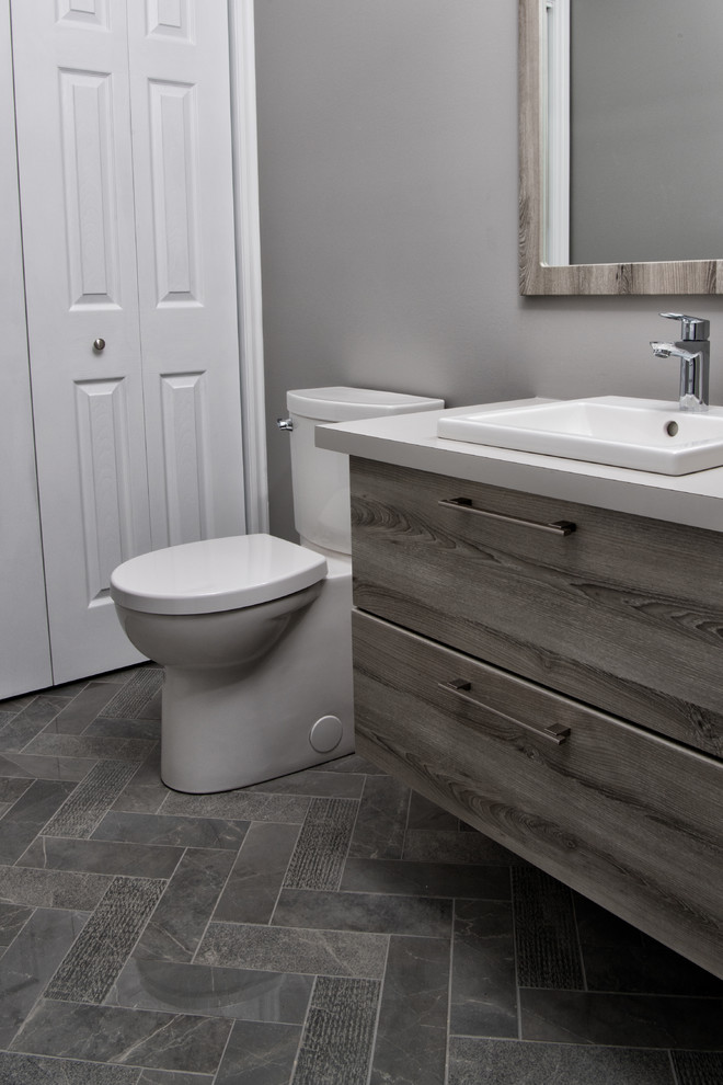Mid-sized country 3/4 bathroom in Ottawa with flat-panel cabinets, distressed cabinets, a two-piece toilet, grey walls, porcelain floors, a drop-in sink, solid surface benchtops and grey floor.