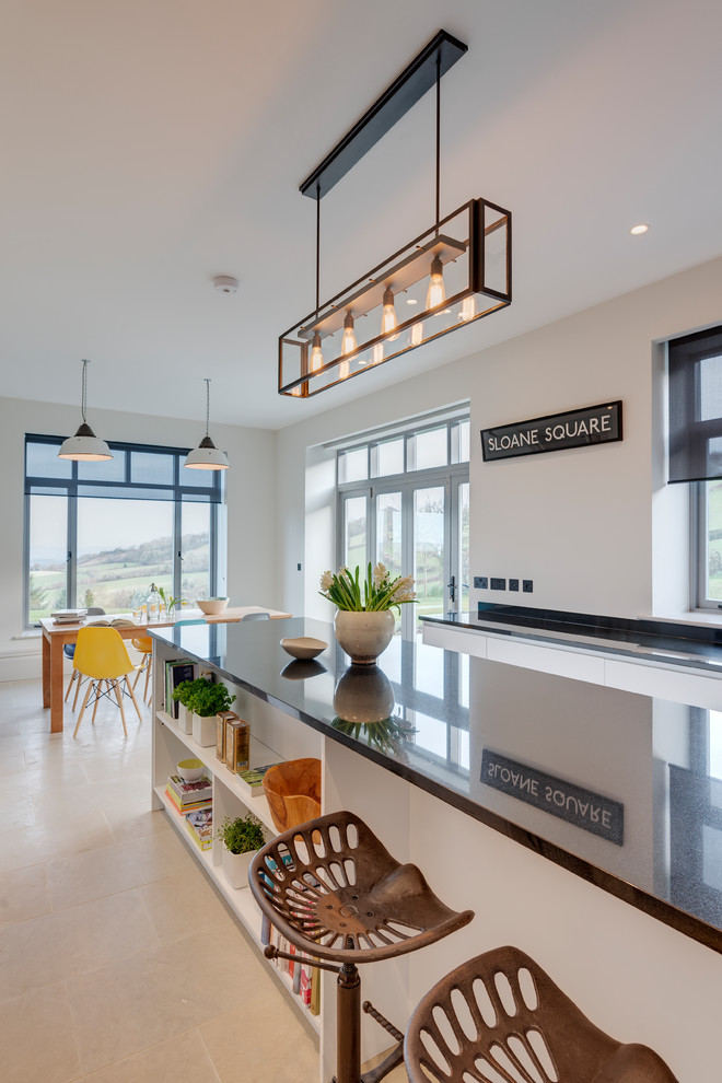 Photo of a large contemporary u-shaped eat-in kitchen in Devon with a farmhouse sink, flat-panel cabinets, white cabinets, granite benchtops, black splashback, stone slab splashback, black appliances, limestone floors, with island and beige floor.