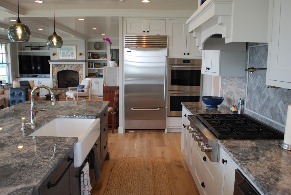 Inspiration for a large beach style u-shaped open plan kitchen in Providence with a farmhouse sink, shaker cabinets, white cabinets, quartz benchtops, grey splashback, subway tile splashback, stainless steel appliances, light hardwood floors, with island, grey benchtop and timber.