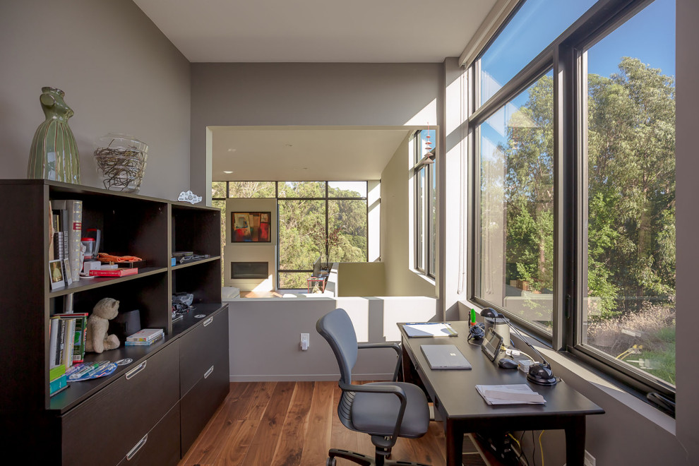 Ejemplo de despacho minimalista con paredes blancas, suelo de madera en tonos medios, chimenea lineal y escritorio independiente