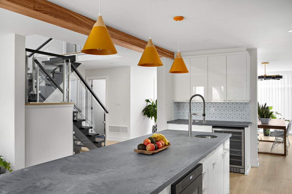 Photo of a contemporary grey and white u-shaped kitchen in Toronto with a submerged sink, flat-panel cabinets, white cabinets, engineered stone countertops, white splashback, ceramic splashback, stainless steel appliances, light hardwood flooring, an island, beige floors, grey worktops and exposed beams.