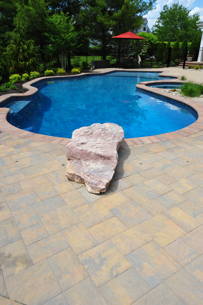 Photo of a mid-sized traditional backyard custom-shaped pool in New York with a hot tub and concrete pavers.