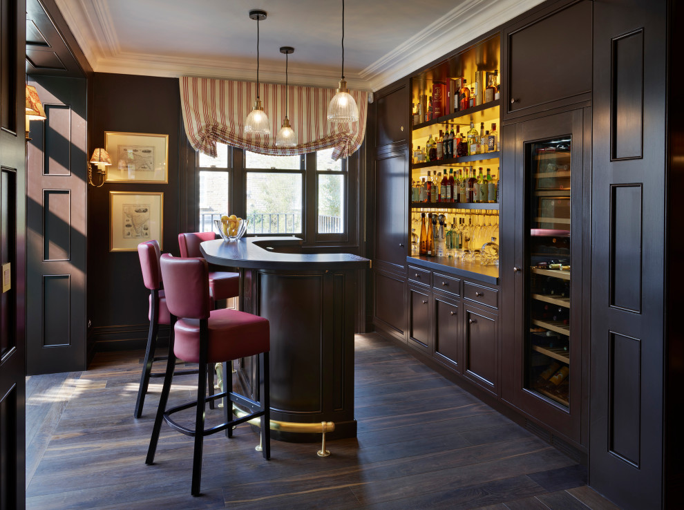 Photo of a mid-sized traditional single-wall seated home bar in London with recessed-panel cabinets, dark wood cabinets, wood benchtops, yellow splashback, glass sheet splashback, dark hardwood floors, brown floor and brown benchtop.
