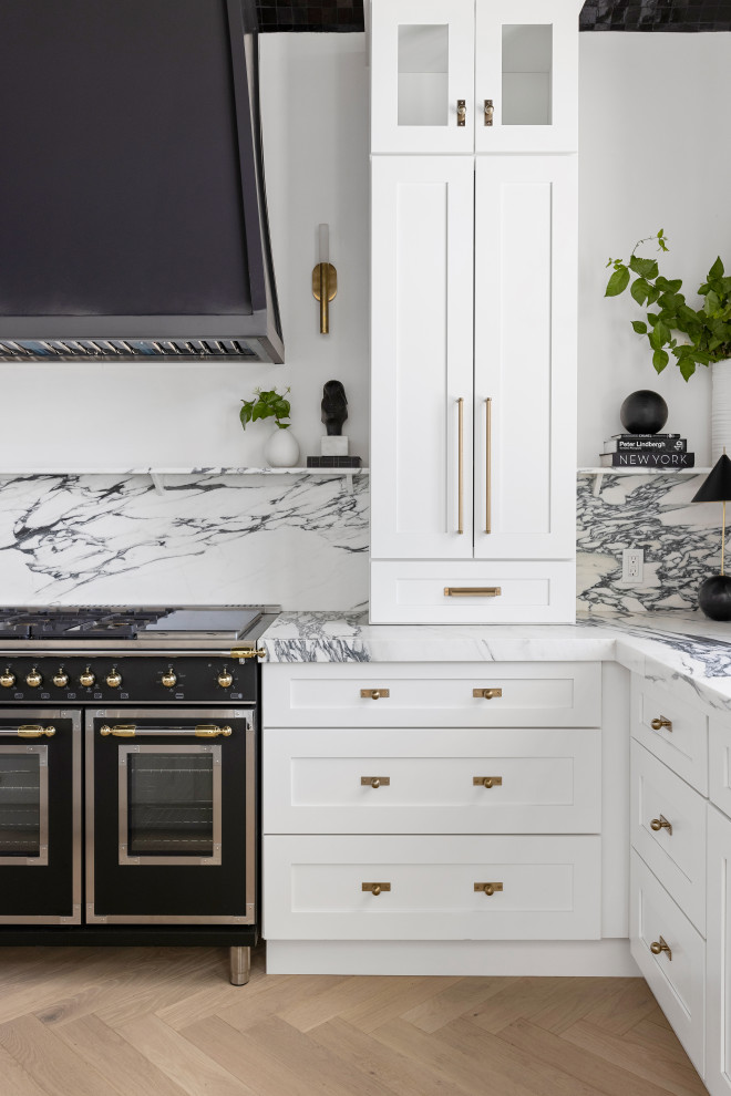 Foto på ett funkis vit kök, med vita skåp, marmorbänkskiva, vitt stänkskydd, stänkskydd i marmor, svarta vitvaror, ljust trägolv, en köksö och brunt golv