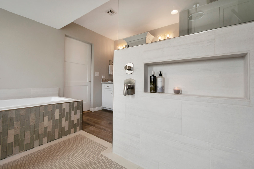 Example of a large transitional master gray tile and porcelain tile porcelain tile and brown floor drop-in bathtub design in Phoenix with shaker cabinets, white cabinets, gray walls, a drop-in sink, quartz countertops and gray countertops