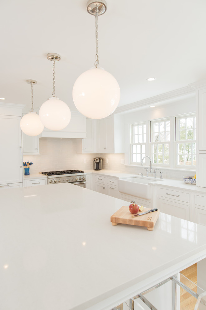 Example of a mid-sized transitional l-shaped medium tone wood floor and brown floor open concept kitchen design in Boston with a farmhouse sink, shaker cabinets, white cabinets, quartz countertops, white backsplash, subway tile backsplash, paneled appliances, an island and white countertops