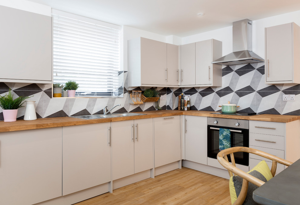 Small contemporary l-shaped eat-in kitchen in Hampshire with flat-panel cabinets, grey cabinets, wood benchtops, cement tile splashback, stainless steel appliances, vinyl floors, a double-bowl sink, grey splashback, no island, beige floor and brown benchtop.