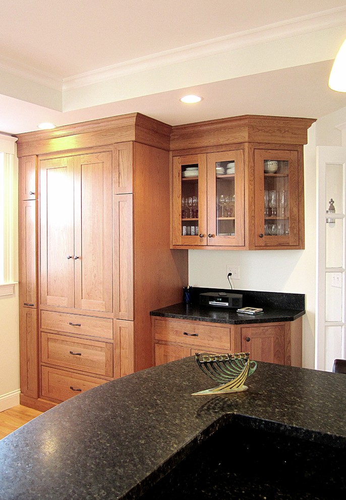 Example of a transitional l-shaped eat-in kitchen design with an undermount sink, recessed-panel cabinets, medium tone wood cabinets, granite countertops, black backsplash, stone slab backsplash and stainless steel appliances