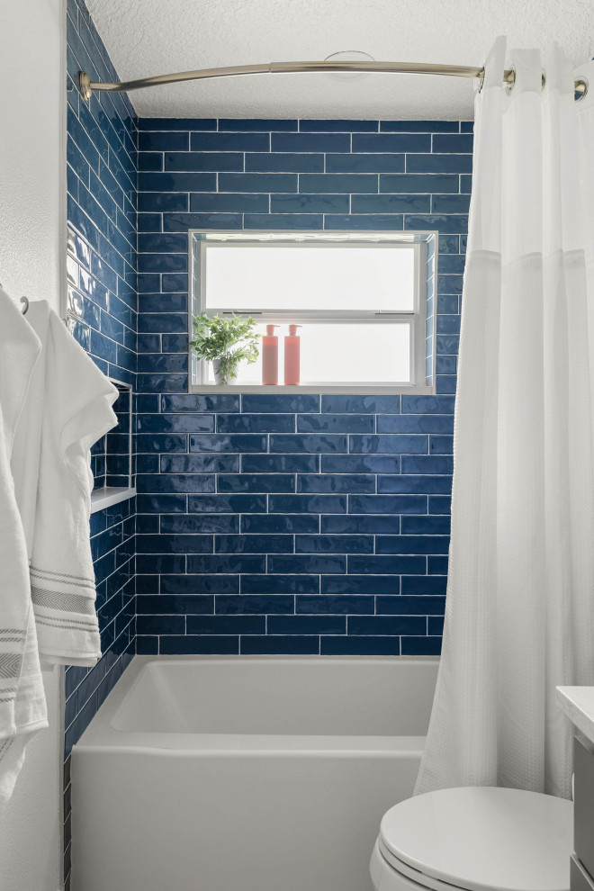 На фото: маленькая детская ванная комната в стиле неоклассика (современная классика) с фасадами с утопленной филенкой, искусственно-состаренными фасадами, накладной ванной, душем над ванной, унитазом-моноблоком, синей плиткой, керамогранитной плиткой, серыми стенами, полом из керамогранита, врезной раковиной, столешницей из искусственного камня, серым полом, шторкой для ванной, белой столешницей, тумбой под одну раковину и напольной тумбой для на участке и в саду