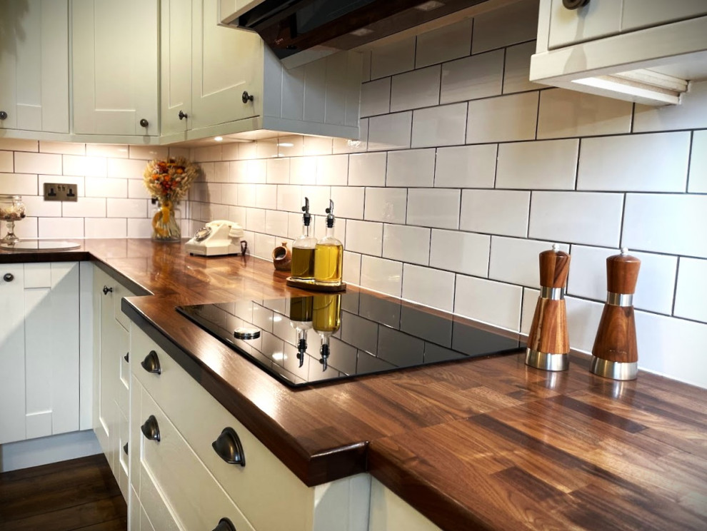 Mid-sized traditional l-shaped separate kitchen in Other with a farmhouse sink, shaker cabinets, white cabinets, wood benchtops, white splashback, black appliances, dark hardwood floors, with island, brown floor and brown benchtop.