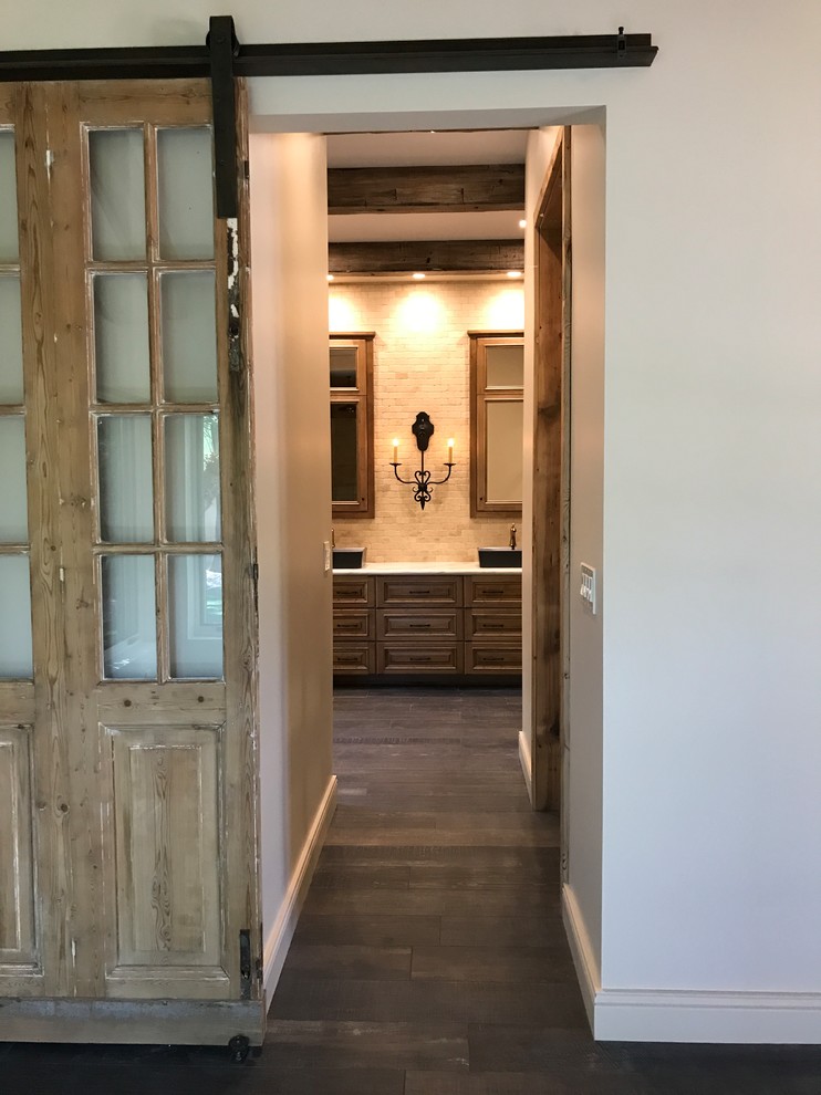 This is an example of a mid-sized mediterranean master bathroom in Phoenix with raised-panel cabinets, dark wood cabinets, a freestanding tub, an alcove shower, a one-piece toilet, beige tile, stone tile, beige walls, dark hardwood floors, a vessel sink, marble benchtops, brown floor and a hinged shower door.