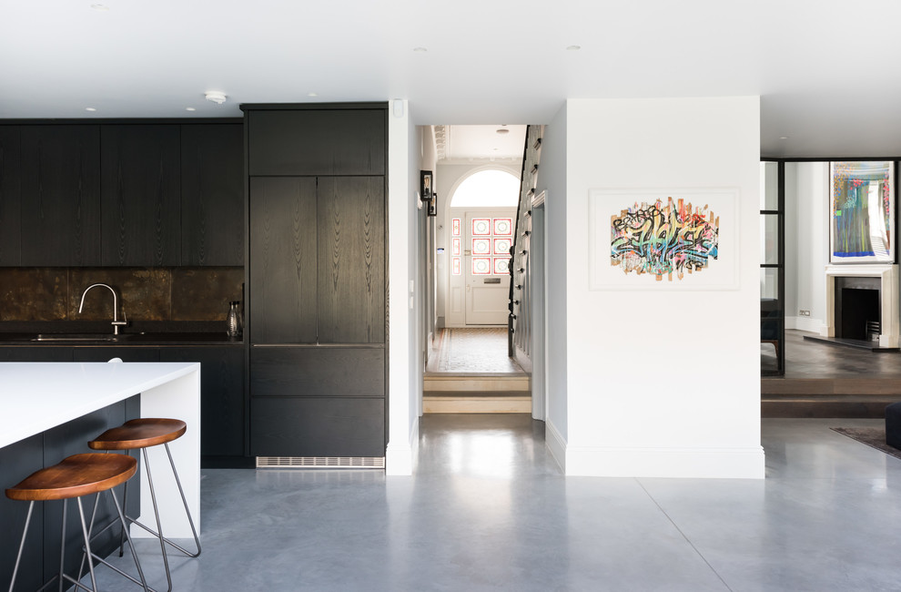 Expansive contemporary l-shaped open plan kitchen in London with a drop-in sink, flat-panel cabinets, dark wood cabinets, quartzite benchtops, multi-coloured splashback, metal splashback, stainless steel appliances, concrete floors, with island, grey floor and white benchtop.