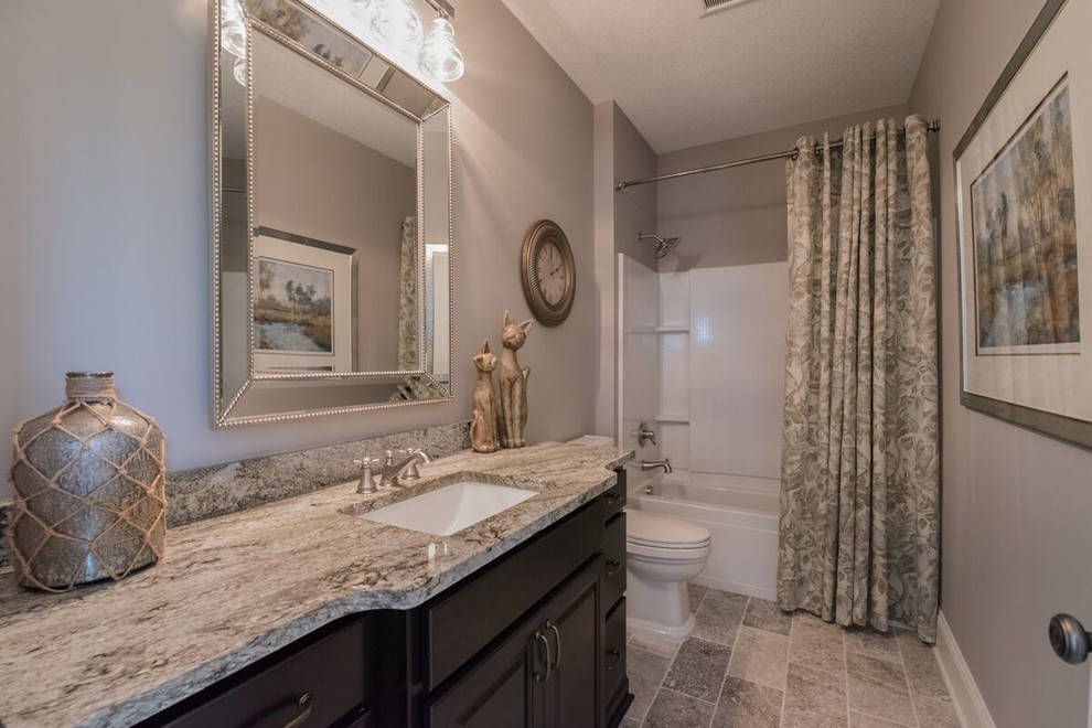 This is an example of a mid-sized transitional 3/4 bathroom in Minneapolis with raised-panel cabinets, white cabinets, an alcove tub, a shower/bathtub combo, a two-piece toilet, gray tile, porcelain tile, grey walls, ceramic floors, an undermount sink, granite benchtops, grey floor and a shower curtain.