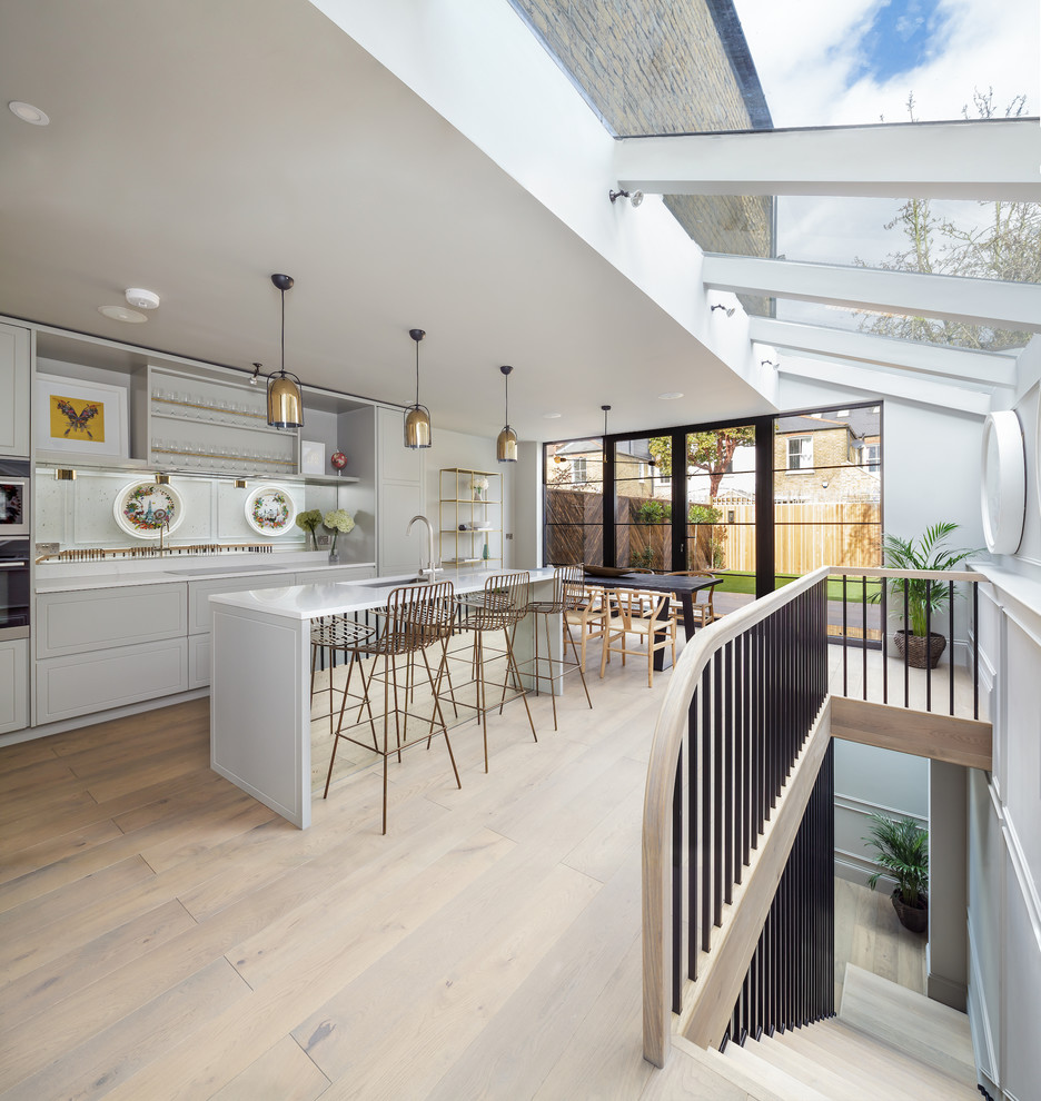 Design ideas for a medium sized contemporary galley kitchen/diner in London with a submerged sink, raised-panel cabinets, grey cabinets, mirror splashback, integrated appliances, light hardwood flooring, an island, beige floors and white worktops.