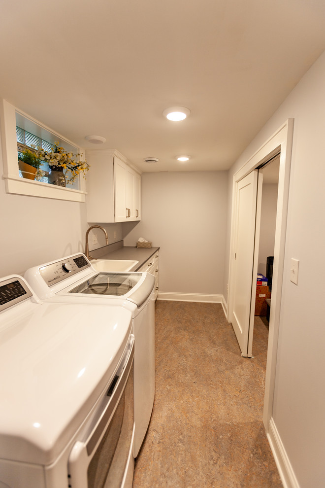 This is an example of a transitional single-wall dedicated laundry room in Minneapolis with a single-bowl sink, recessed-panel cabinets, white cabinets, solid surface benchtops, grey walls, linoleum floors, a side-by-side washer and dryer, beige floor and grey benchtop.