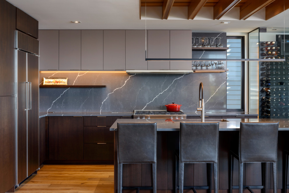 This is an example of a mid-sized contemporary l-shaped kitchen in Seattle with an undermount sink, flat-panel cabinets, dark wood cabinets, grey splashback, stainless steel appliances, medium hardwood floors, with island, brown floor and grey benchtop.