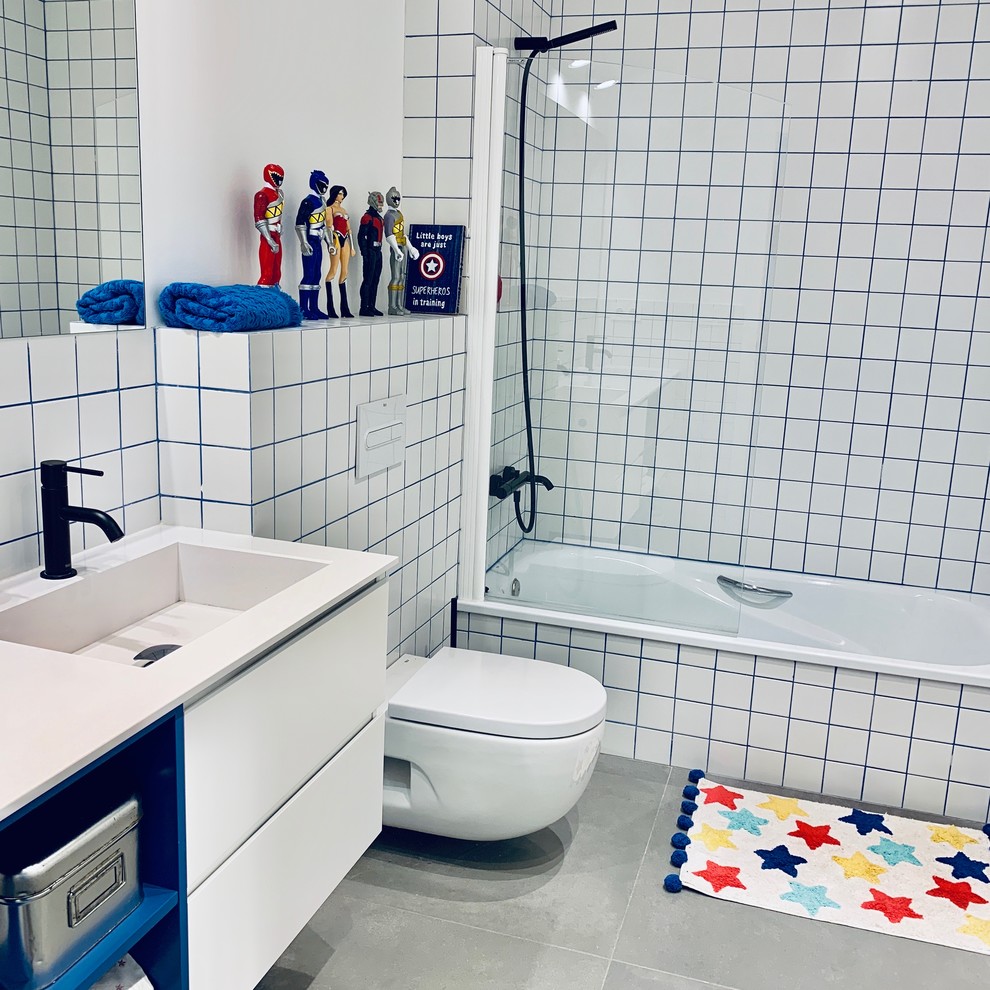Photo of a mid-sized modern 3/4 bathroom in Other with recessed-panel cabinets, white cabinets, an alcove tub, an alcove shower, a wall-mount toilet, white tile, ceramic tile, white walls, porcelain floors, a wall-mount sink, grey floor, a hinged shower door and white benchtops.