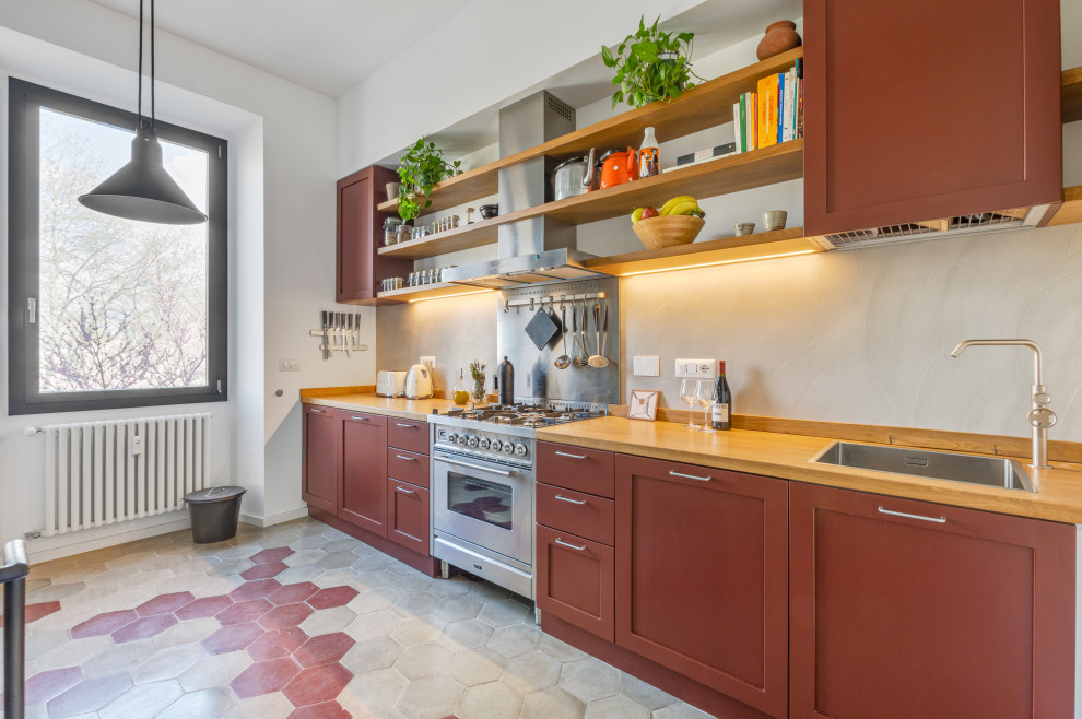 This is an example of a large contemporary single-wall kitchen/diner in Rome with a built-in sink, recessed-panel cabinets, red cabinets, wood worktops, grey splashback and cement flooring.