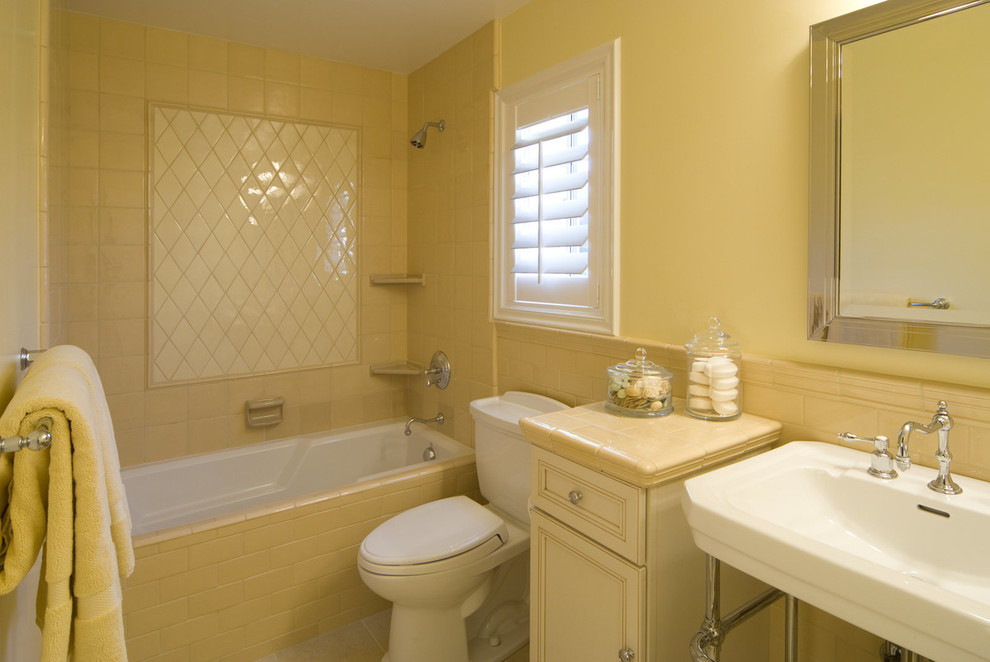 Inspiration for a mid-sized traditional kids bathroom in San Francisco with recessed-panel cabinets, red cabinets, a shower/bathtub combo, a two-piece toilet, ceramic tile, yellow walls, ceramic floors, a pedestal sink, tile benchtops and beige tile.