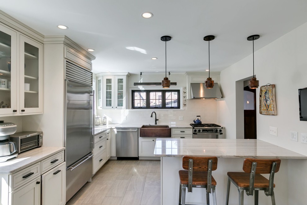 Country l-shaped kitchen in Philadelphia with a farmhouse sink, recessed-panel cabinets, white cabinets, marble benchtops, white splashback, ceramic splashback, stainless steel appliances, ceramic floors and a peninsula.