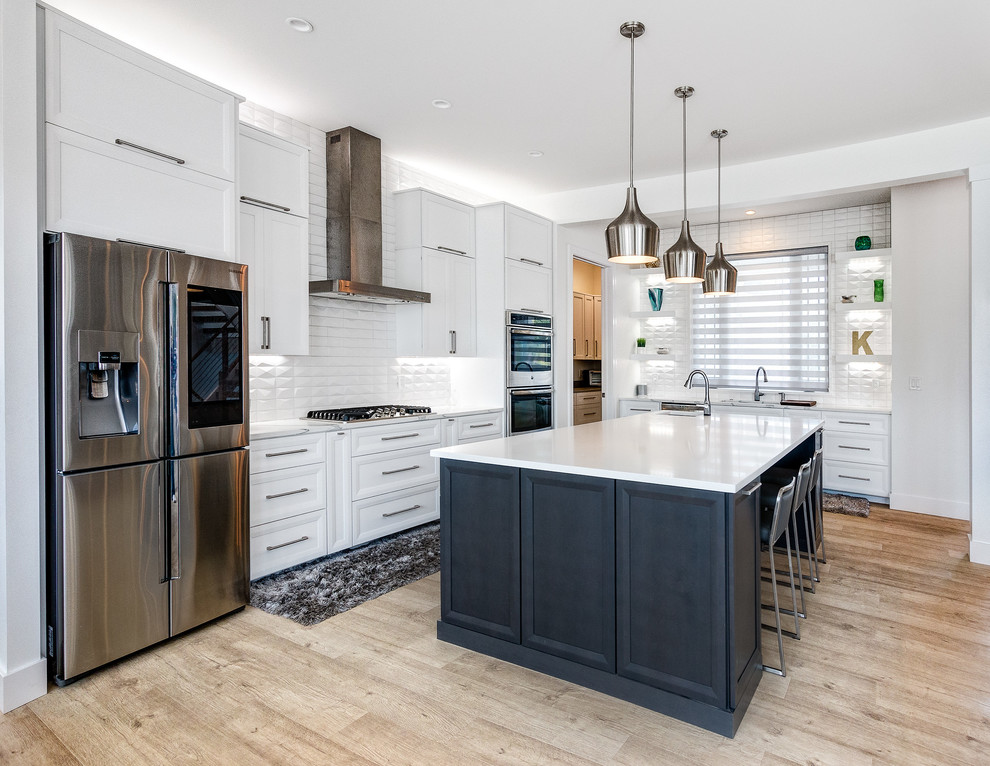 This is an example of a transitional l-shaped kitchen in Cleveland with shaker cabinets, white cabinets, white splashback, stainless steel appliances, light hardwood floors and with island.