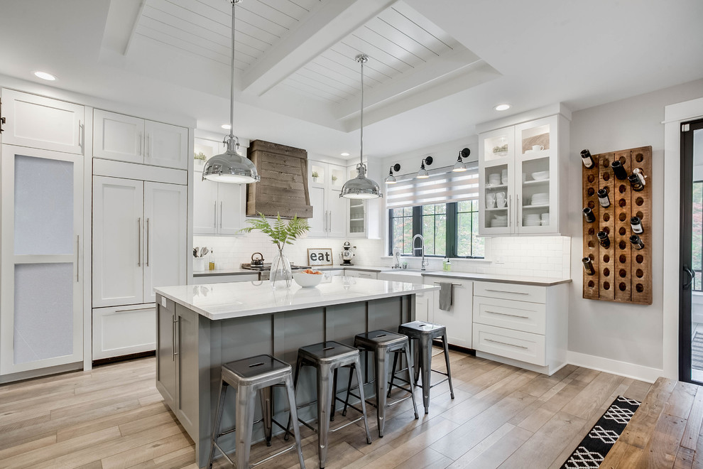 Inspiration for a country l-shaped eat-in kitchen in Grand Rapids with a farmhouse sink, shaker cabinets, white cabinets, white splashback, subway tile splashback, panelled appliances, with island, brown floor and white benchtop.