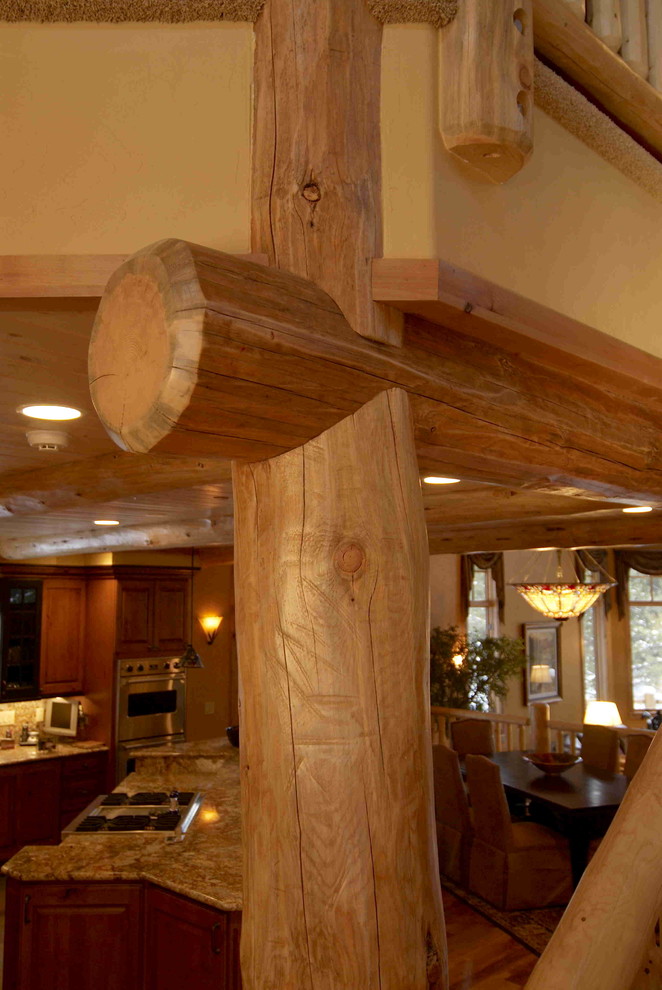 Example of a mid-sized mountain style l-shaped medium tone wood floor eat-in kitchen design in Denver with brown cabinets, granite countertops, an island, an undermount sink, raised-panel cabinets, beige backsplash, stone slab backsplash and stainless steel appliances
