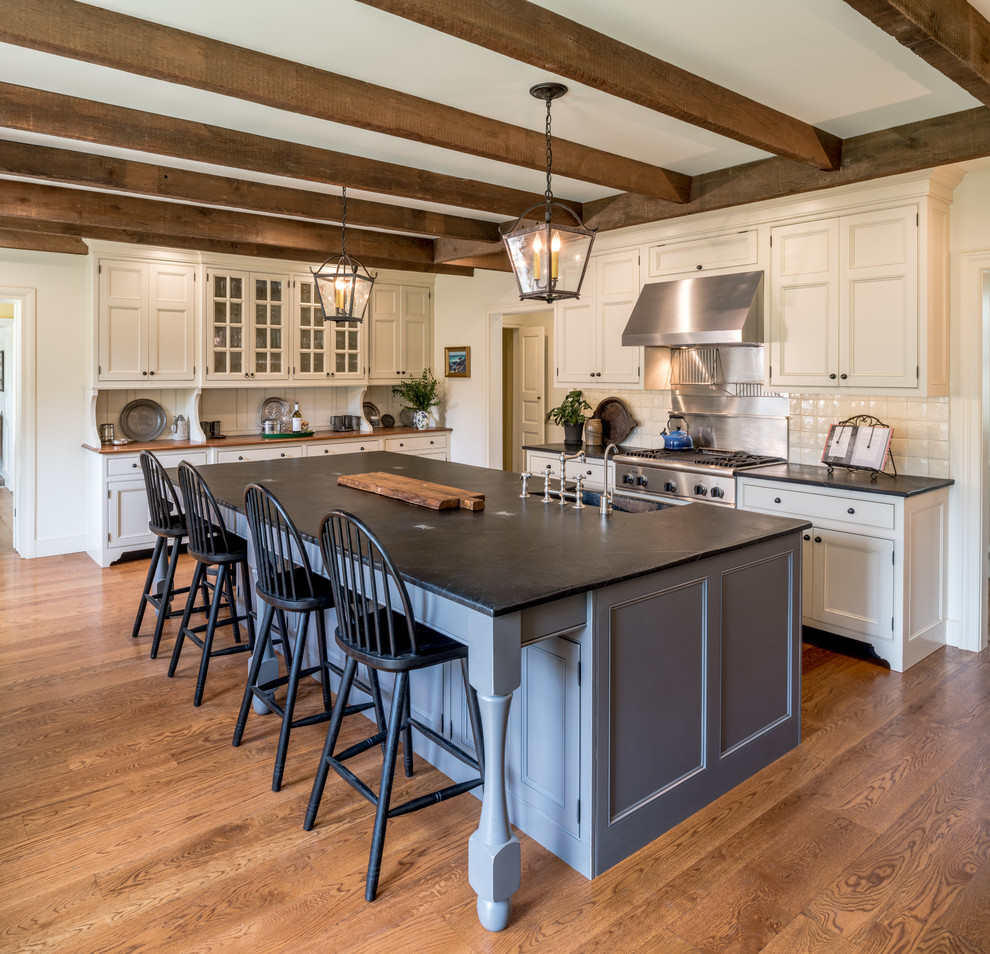 Huge elegant l-shaped medium tone wood floor and brown floor kitchen photo in Philadelphia with a farmhouse sink, beaded inset cabinets, beige cabinets, soapstone countertops, beige backsplash, stainless steel appliances, an island and black countertops