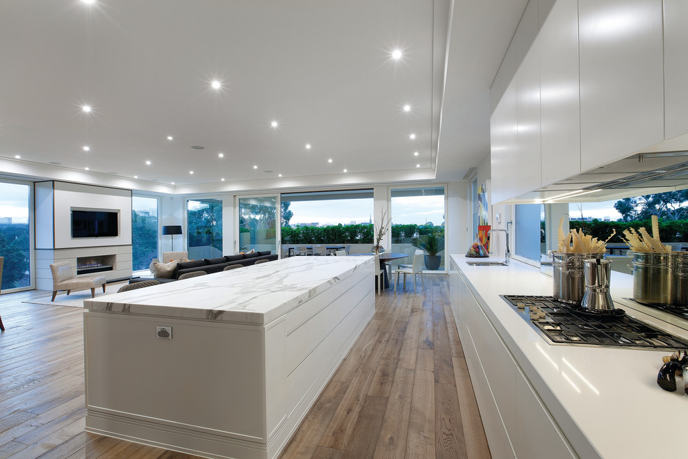 Modern open plan kitchen in Melbourne with flat-panel cabinets, white cabinets, marble benchtops and mirror splashback.