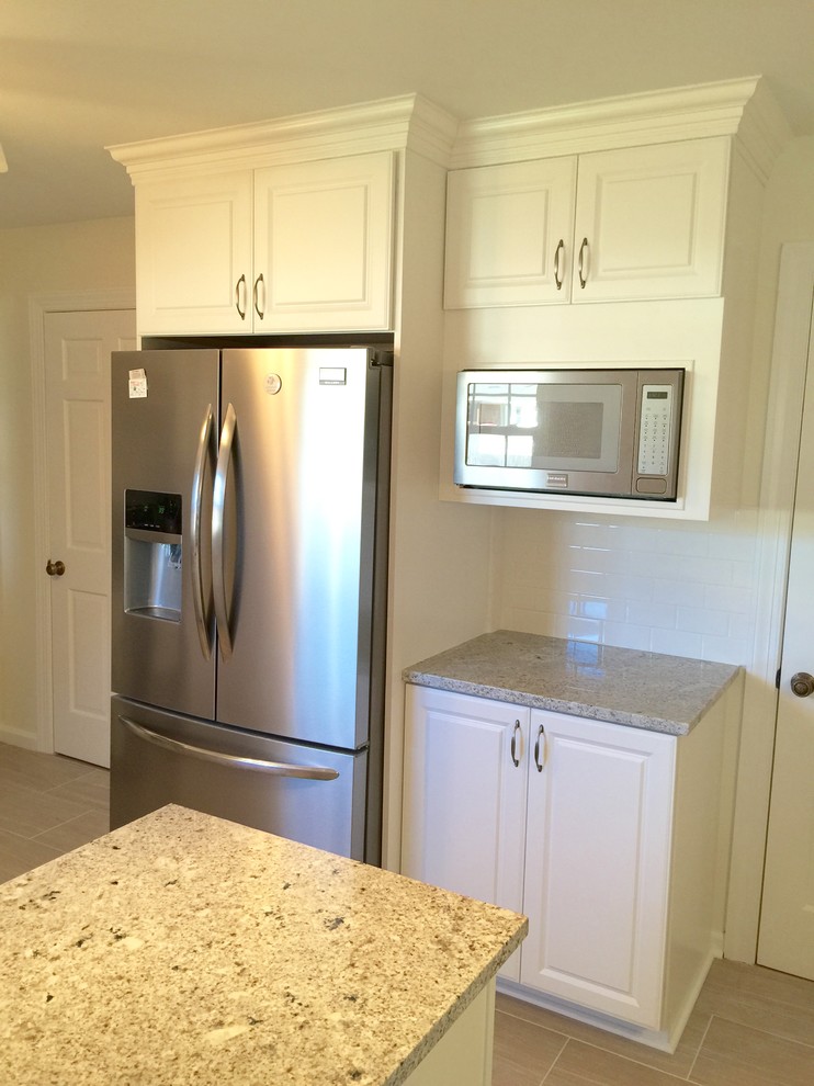 Enclosed kitchen - mid-sized transitional u-shaped porcelain tile enclosed kitchen idea with an undermount sink, raised-panel cabinets, white cabinets, granite countertops, white backsplash, subway tile backsplash, stainless steel appliances and a peninsula